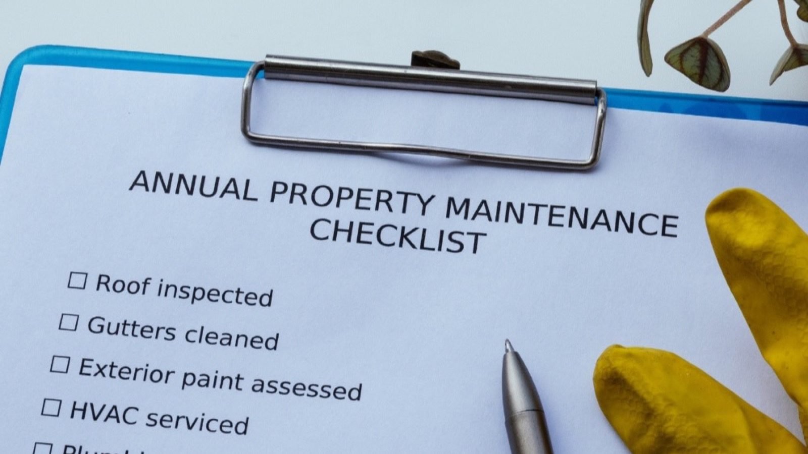 An annual property maintenance checklist on a clipboard beside work gloves and a pen